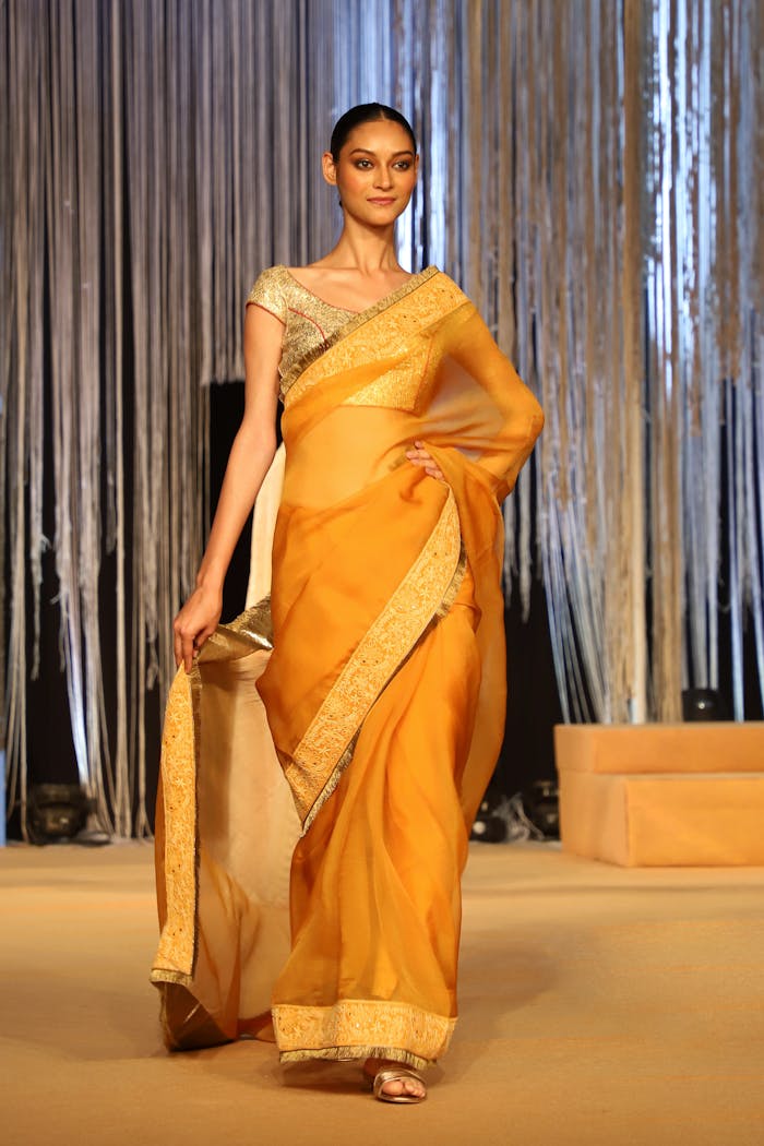 Model in a yellow saree walks the ramp at an indoor fashion event in India.